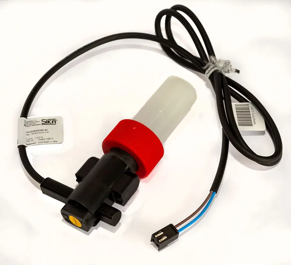 Daikin Durchfluss-Schalter mit rotem und schwarzem Gehäuse, verbunden mit einem Kabel für elektrische Anschlüsse, auf weißem Hintergrund.